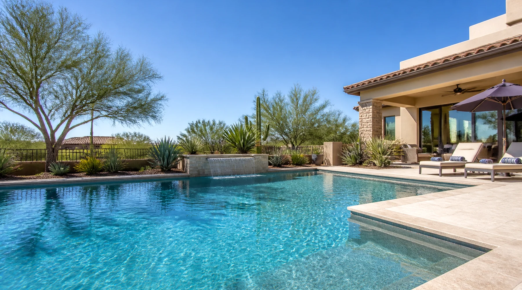 Arizona backyard swimming pool with a stone patio and desert landscaping under a clear sky