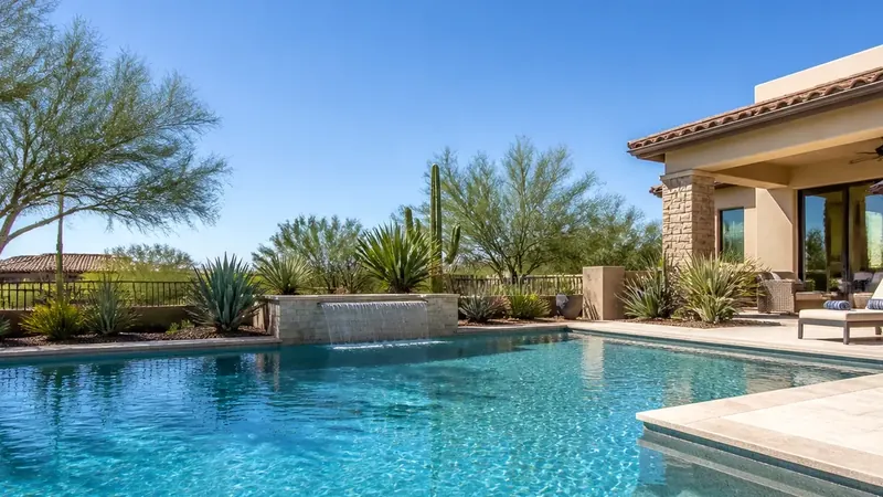 An Arizona backyard swimming pool in full sun with desert trees and a blue sky.